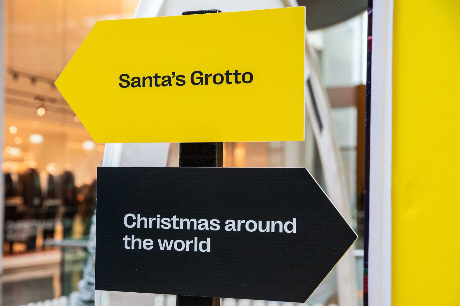 Part of the Yellow Santa 'pop-up' – a post with two signs. One says "Santa's Grotto" pointing left, the other says "Christmas around the world" pointing right.
