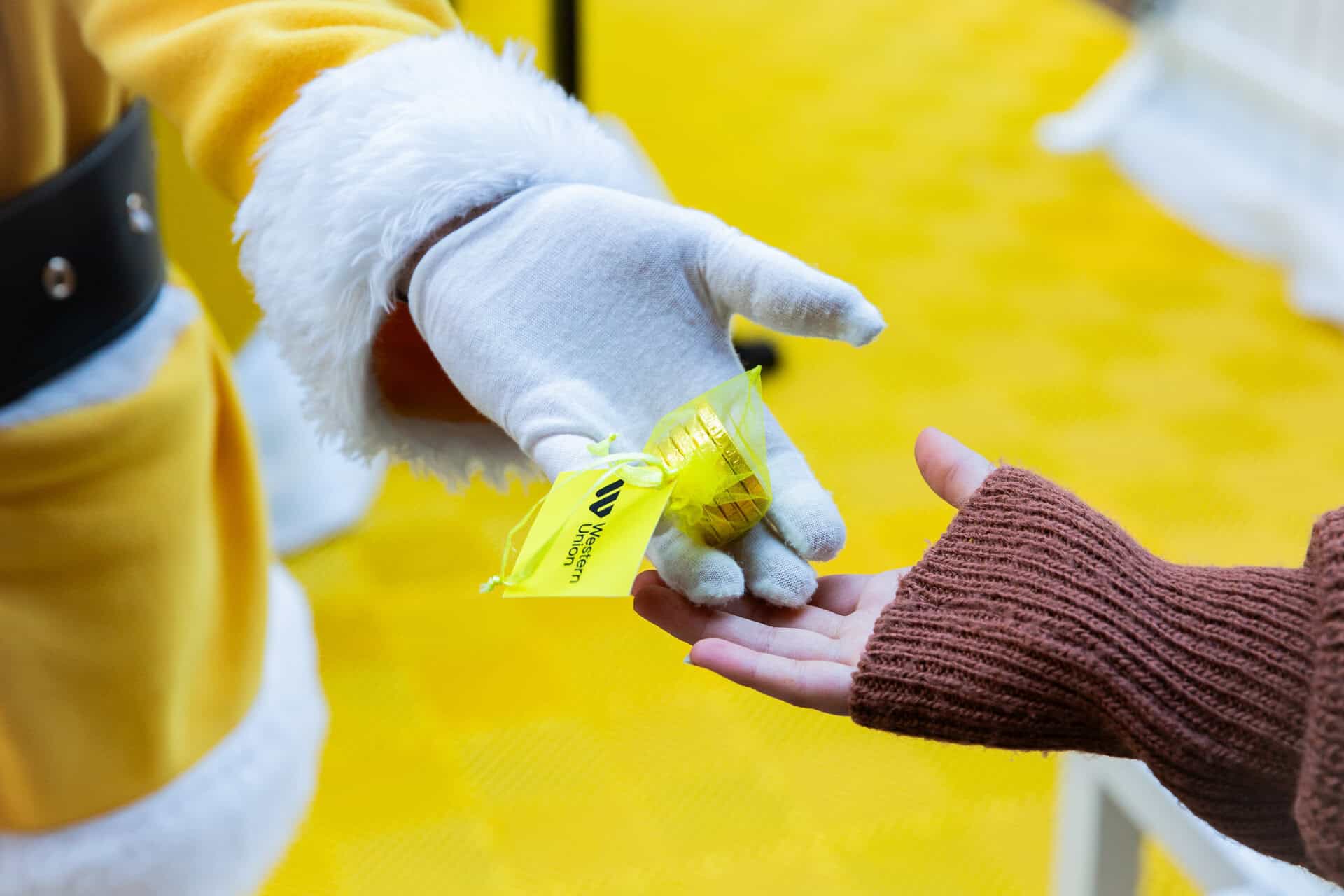 Yellow Santa passing someone a bag of chocolate coins.