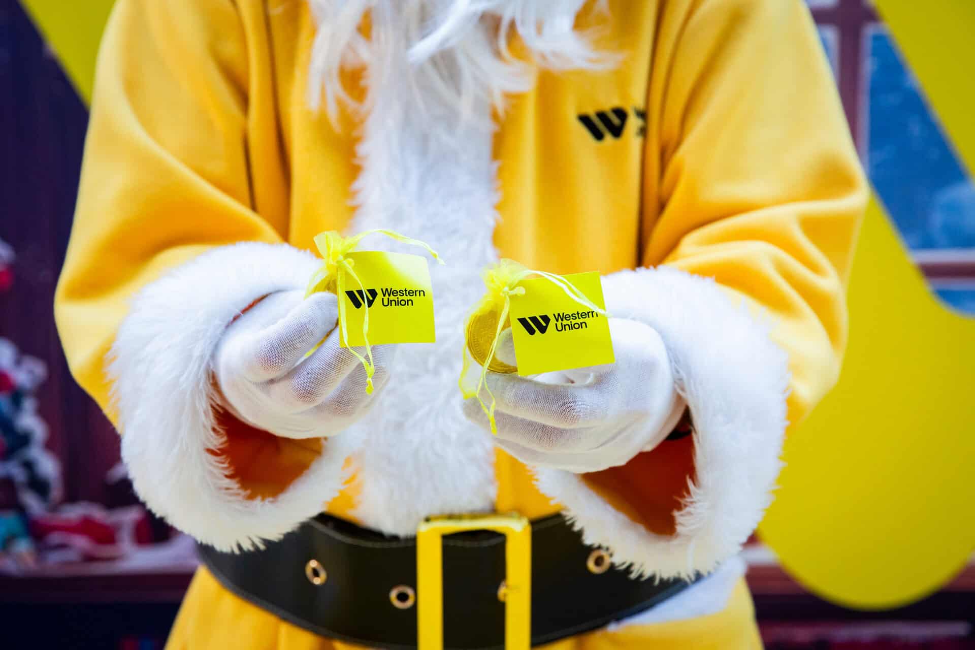 Yellow Santa holding golden chocolate coins to the camera.
